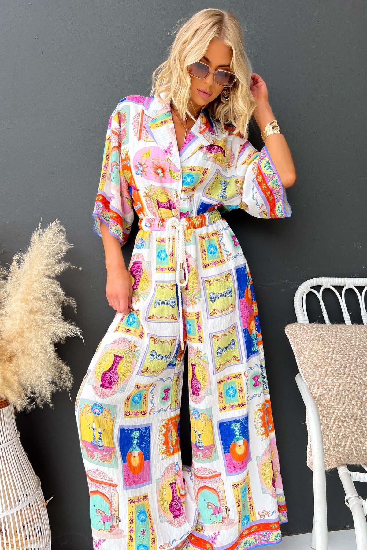 Model wearing Perrin Jumpsuit with colorful prints, collar, button-up front, and relaxed fit, styled with sunglasses.