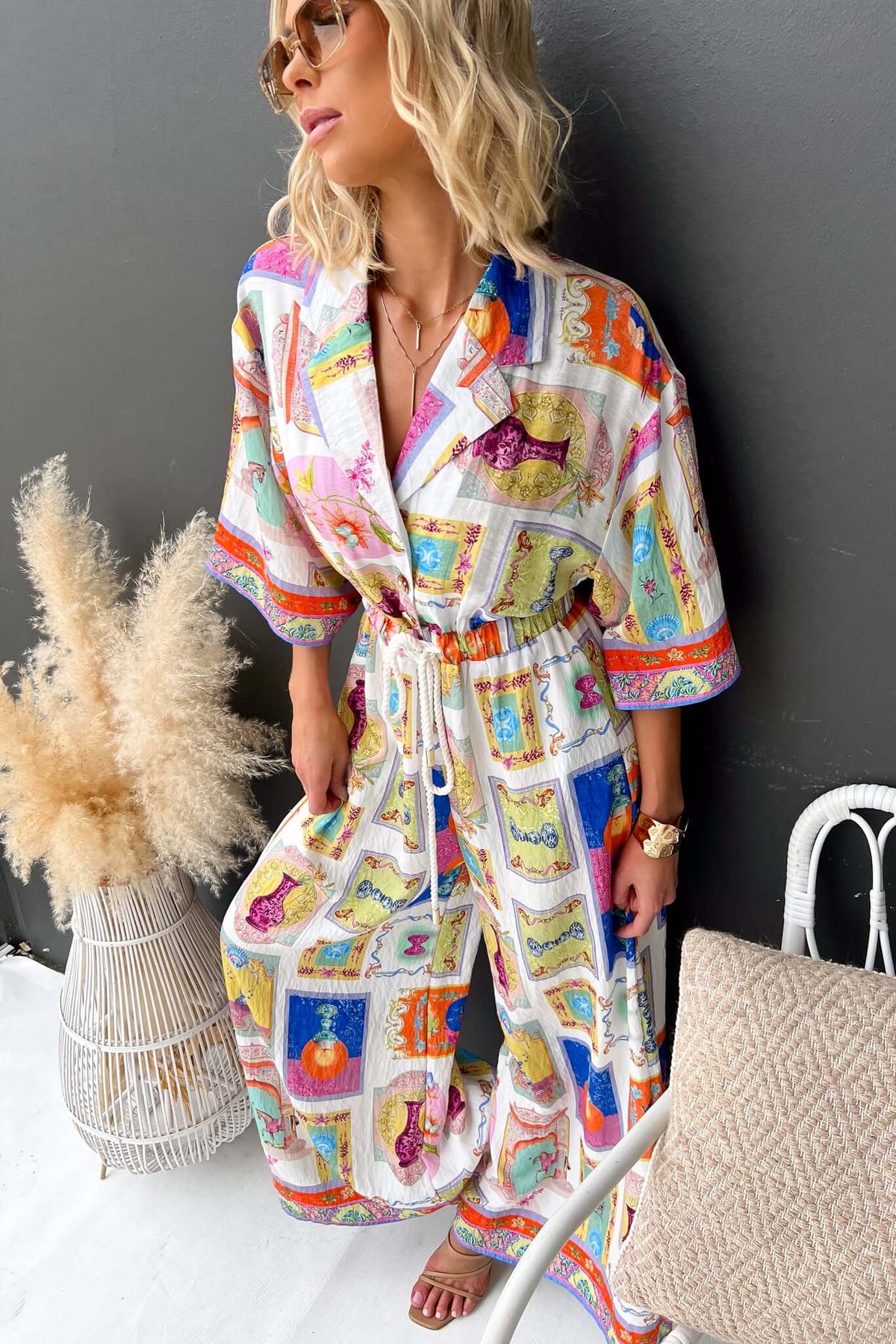 Model wearing colorful Perrin jumpsuit with collar, button-up front, elastic waistband, and pockets in relaxed fit.