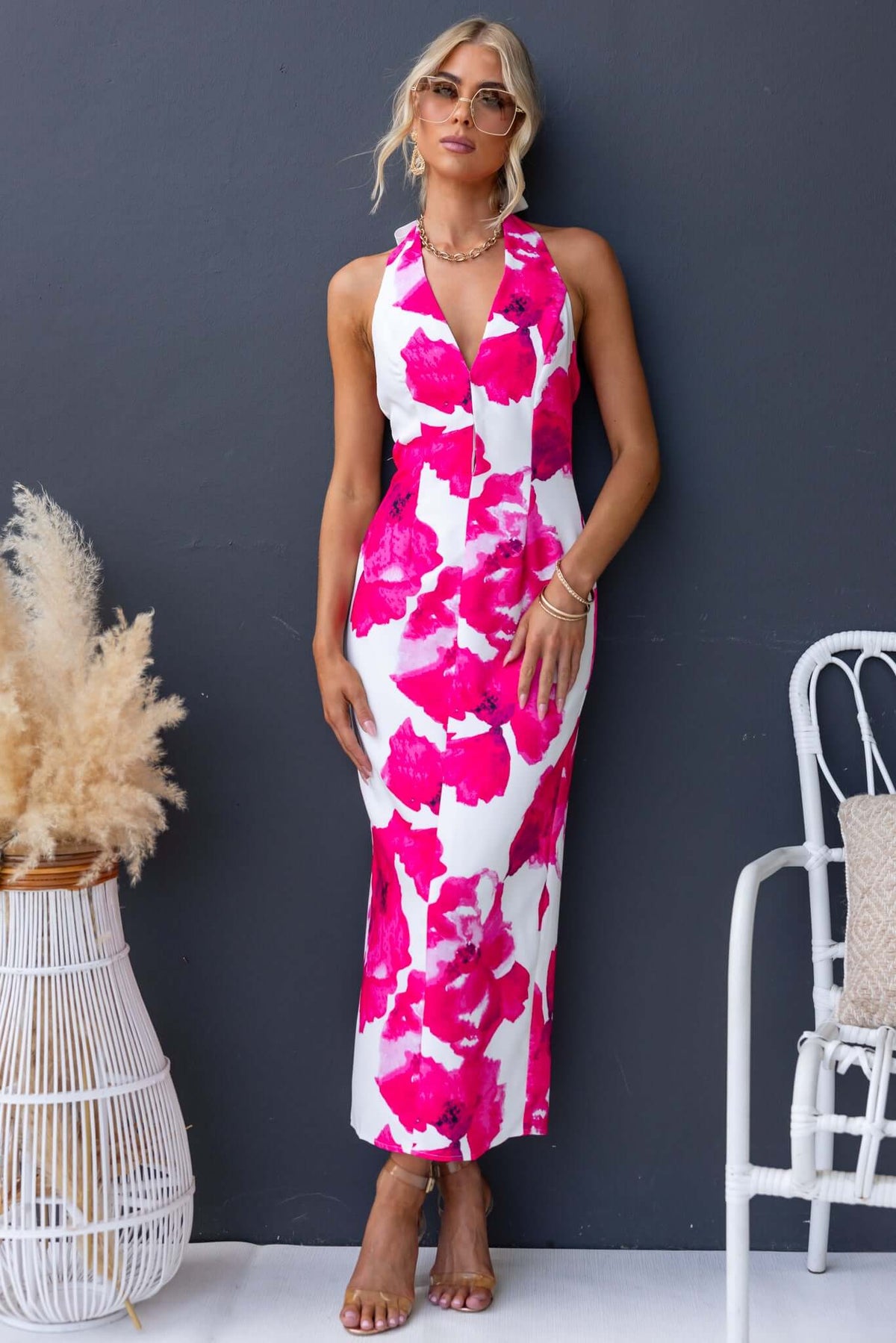 Model wearing the Pianni Maxi Dress with tie halter neckline and pink floral pattern against a dark background.