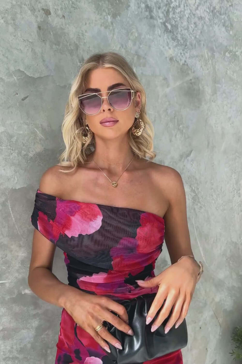 Fashionable woman in one-shoulder maxi dress, floral print, sunglasses, and accessories, perfect for summer outings.