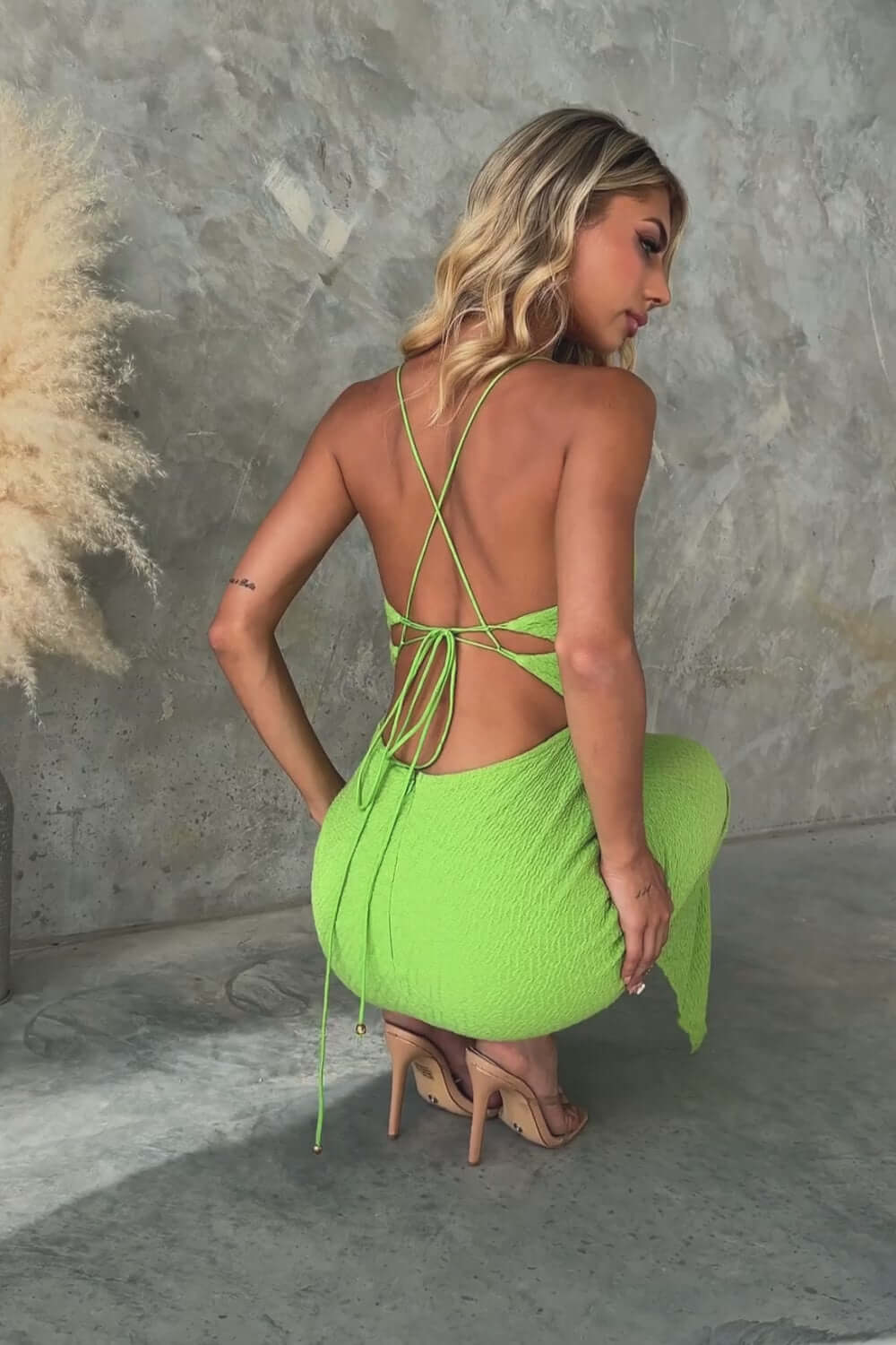 Woman in green Massimo maxi dress with adjustable tie straps, showing back view, in a stylish indoor setting.