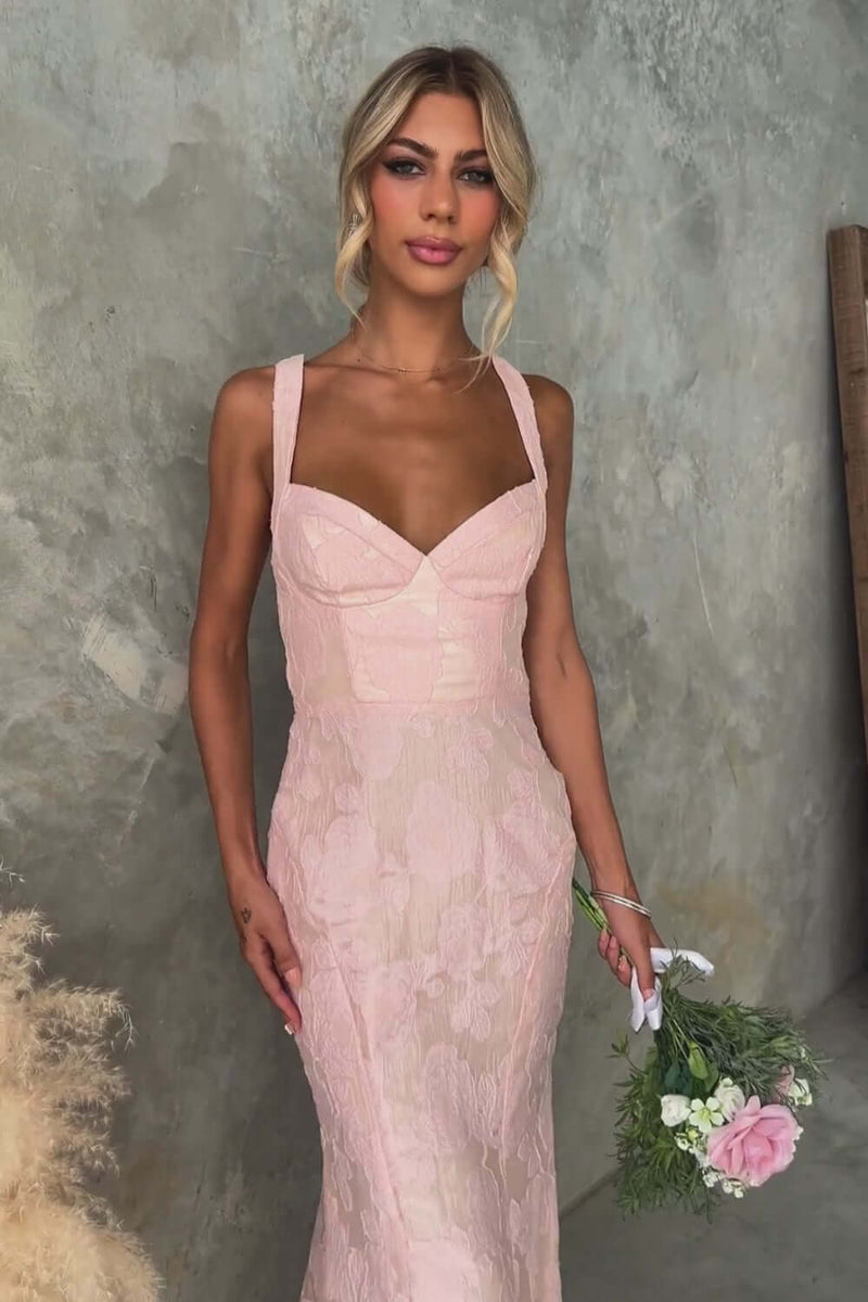 Model in a pink lace maxi dress with a fitted silhouette and holding a bouquet.