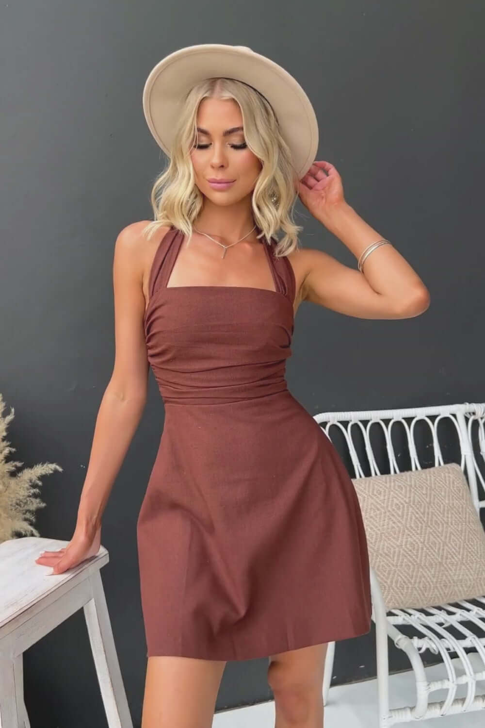Quade Dress featuring tie halter neckline, back zip closure, and a rich brown color, styled with a fashionable hat.
