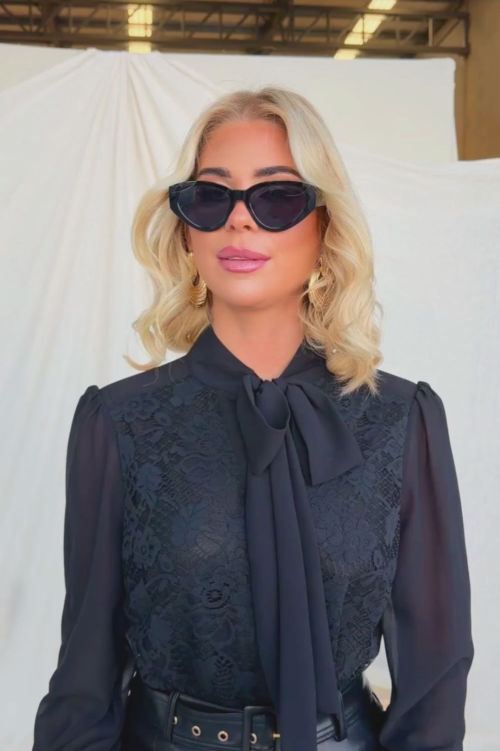 Model wearing the Elijah Shirt with lace detail and tie neckline, styled with sunglasses and elegant makeup.