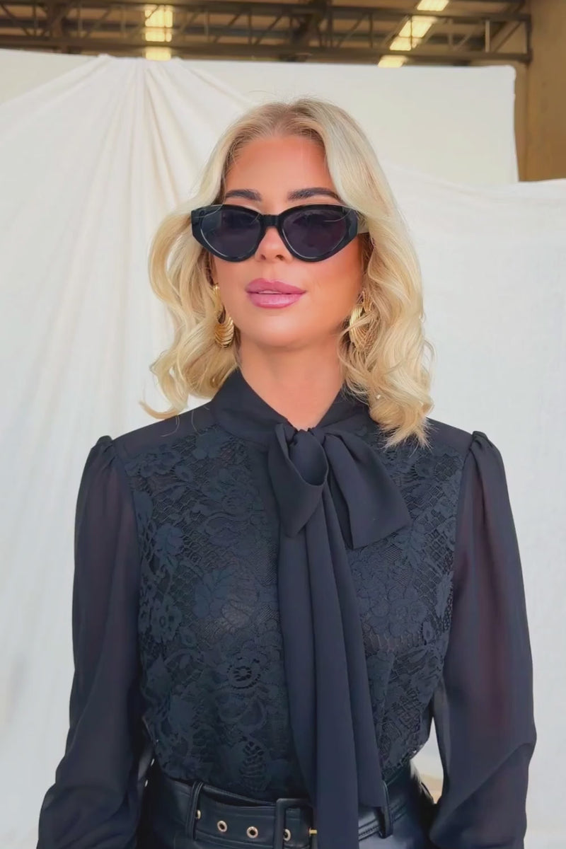 Model wearing the Elijah Shirt with lace detail and tie neckline, styled with sunglasses and elegant makeup.
