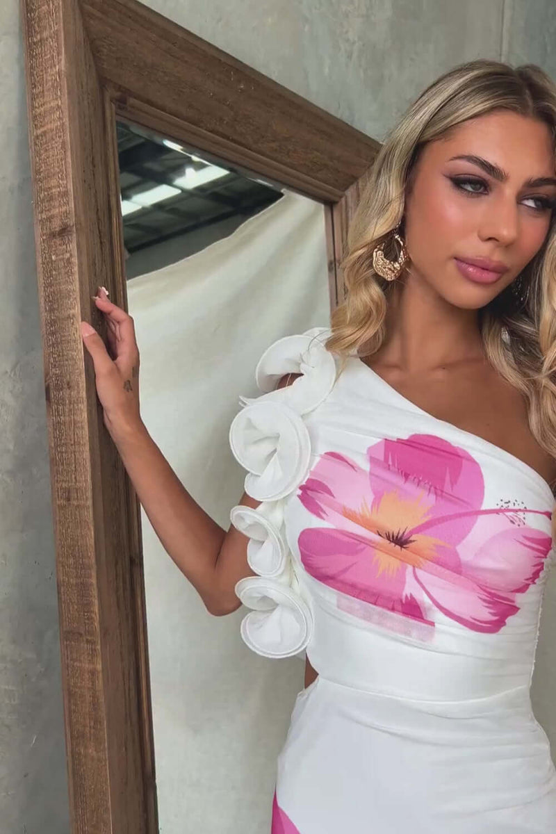Model wearing a stylish one-shoulder maxi dress with floral print and ruffle detail, posing in front of a mirror.
