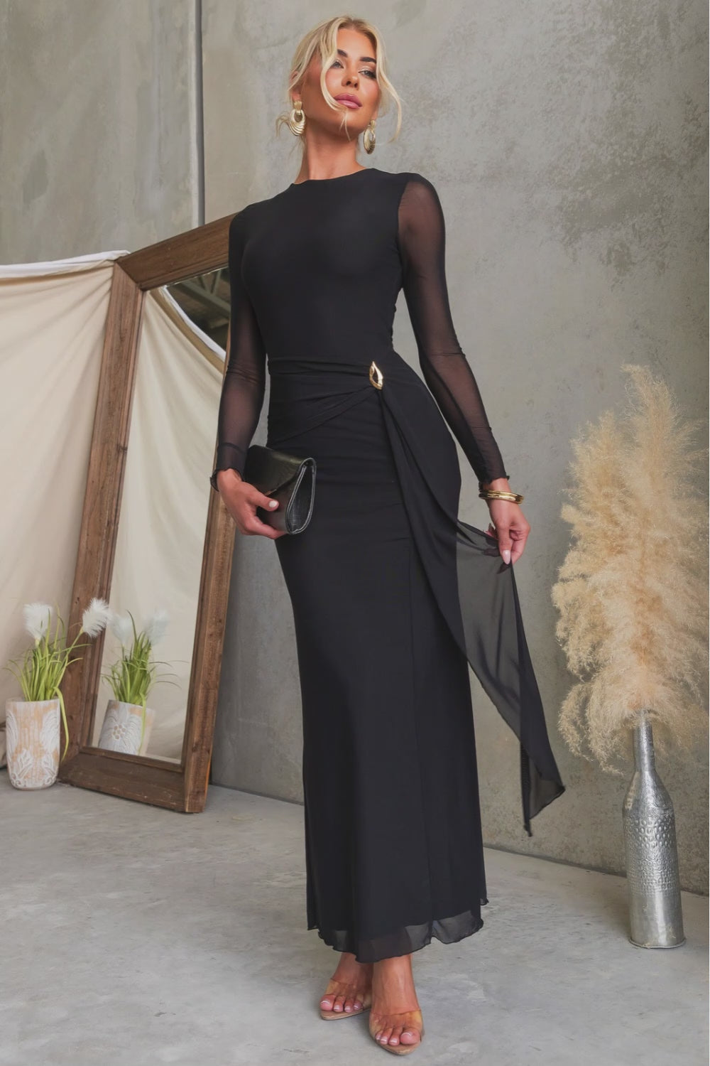 Stunning woman wearing the La Rose Maxi Dress with round neckline and gold hardware, styled with a black clutch.
