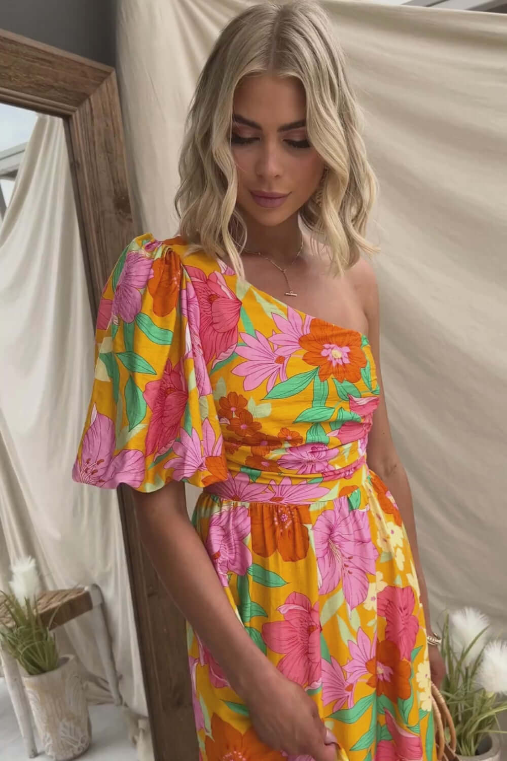 Model wearing Woran Midi Dress, a colorful floral print one-shoulder gown with puff sleeve design.