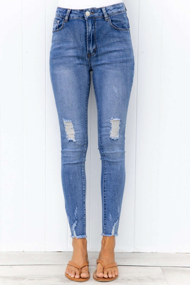 Qilli Jeans - Distressed blue denim jeans with rip details and raw hem, featuring a standard fit and stretchy material.