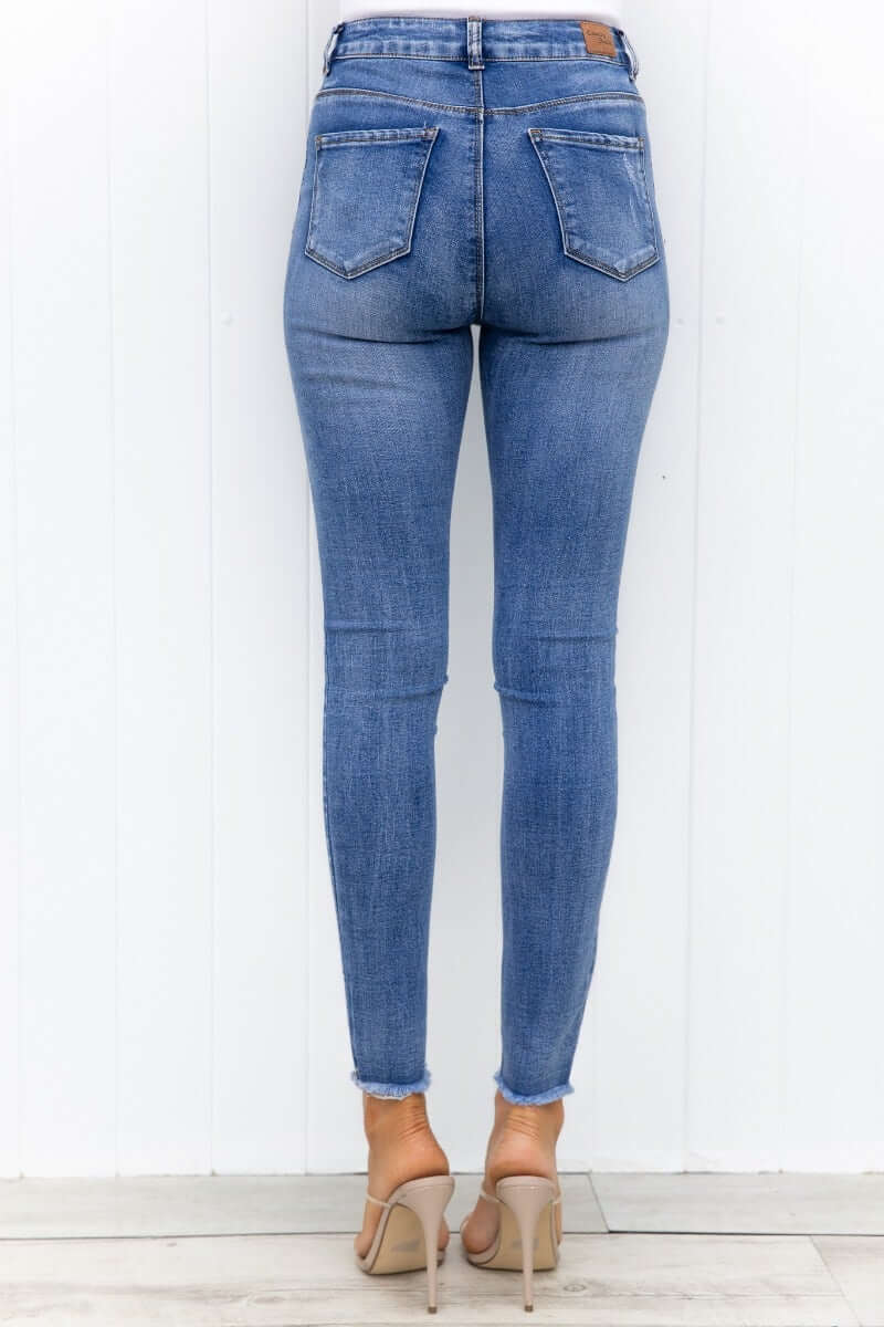 Back view of Qilli Jeans featuring distressed details, raw hem, and standard fit in light wash denim.