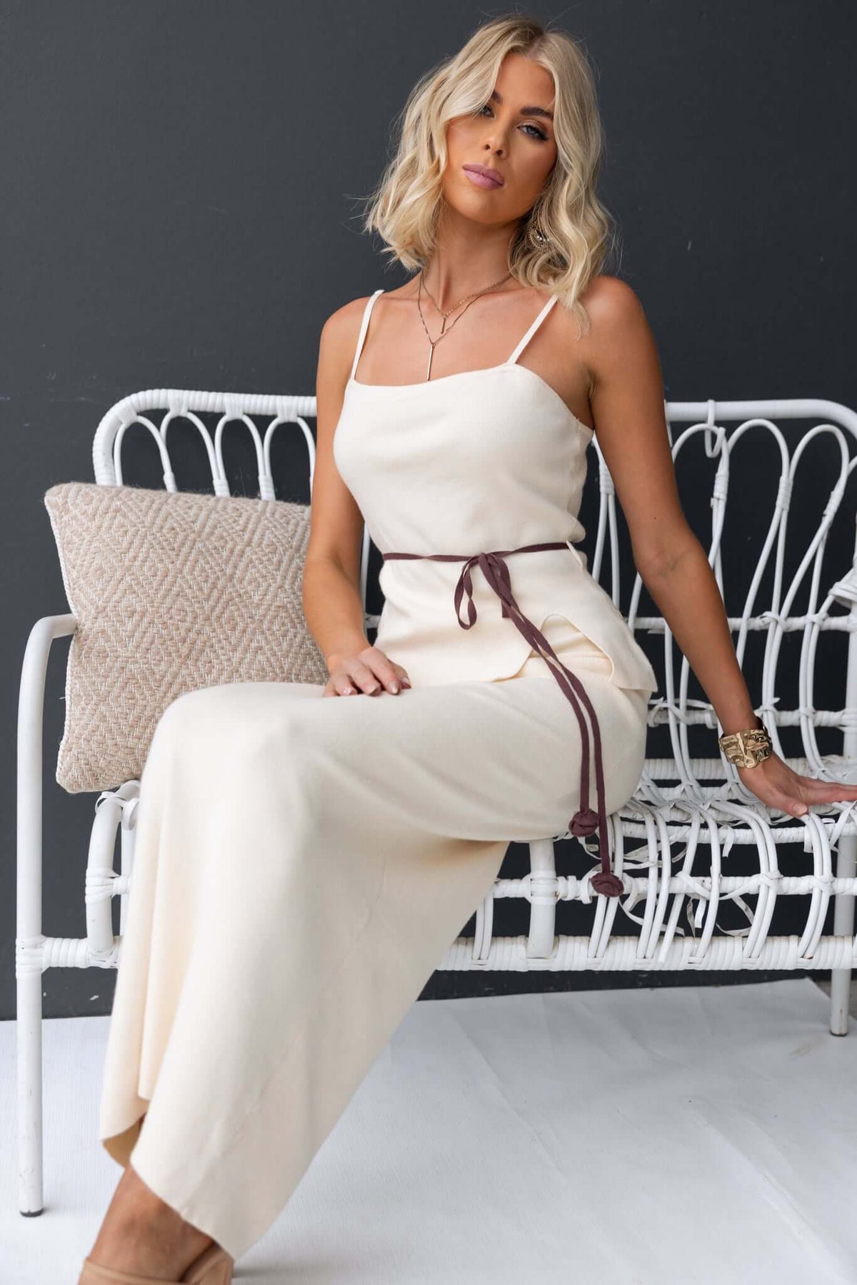 Qarmy Maxi Skirt in cream, mid-high waist, stretch knit material styled with a brown belt, model sitting on a white chair.
