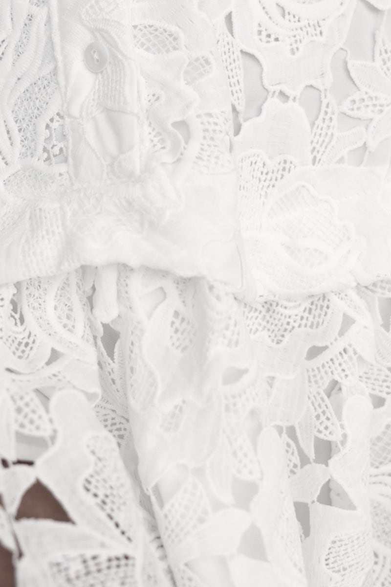 Close-up of soft white lace fabric with intricate floral patterns, showcasing the detail of the Javier Dress.