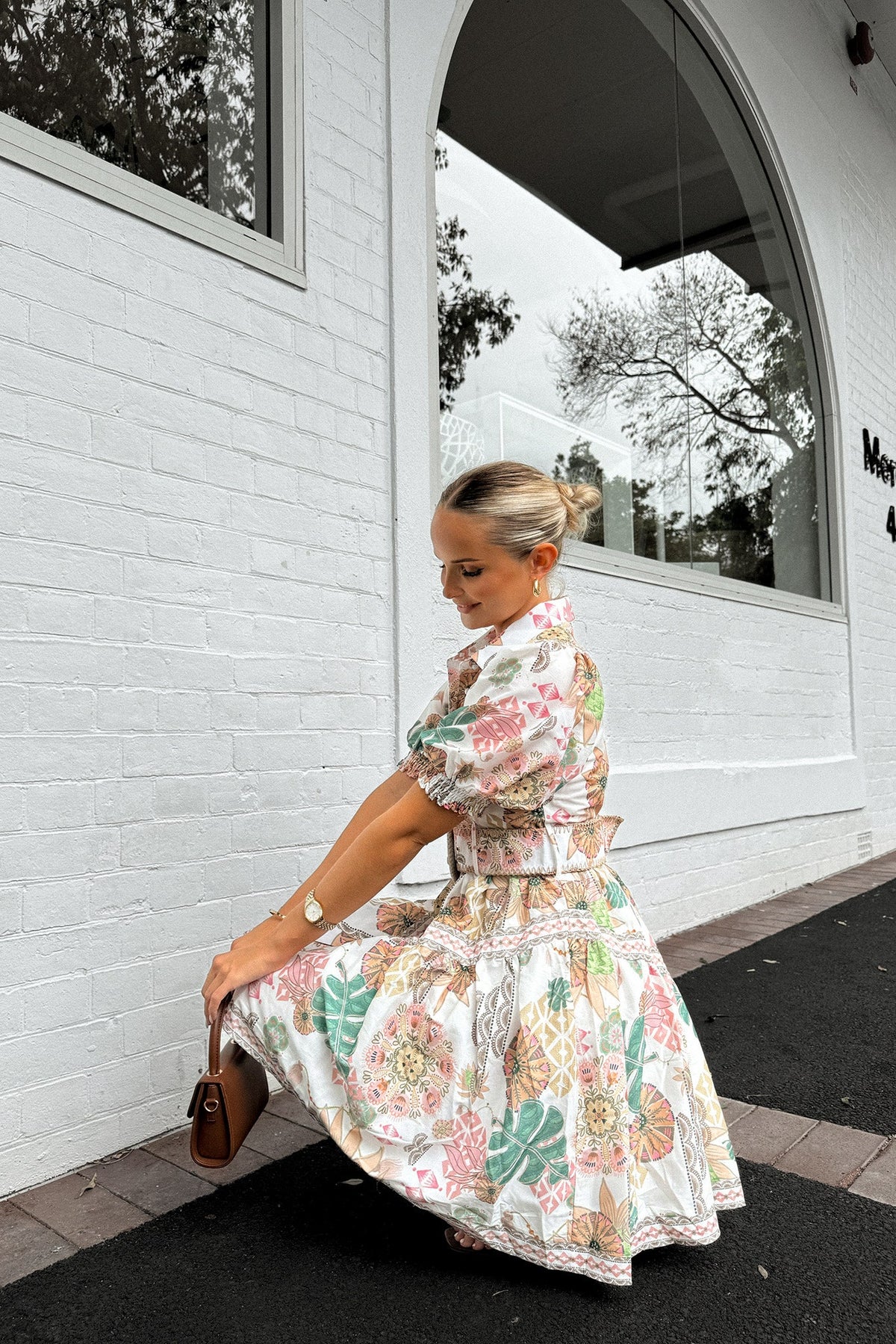 Model wearing the Ember Dress, a floral print dress with a high neckline and removable belt, on a city sidewalk.