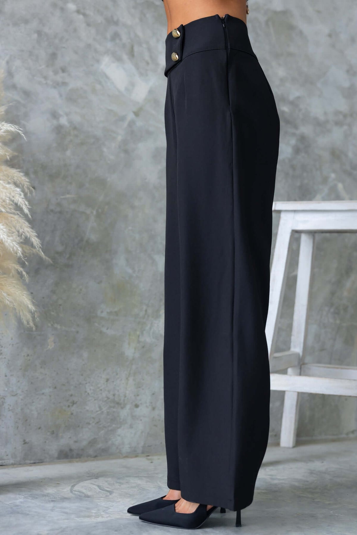 Side view of black Roan Pants with mid-high waist, faux buttons, and invisible side zip, perfect for a chic and elegant look.