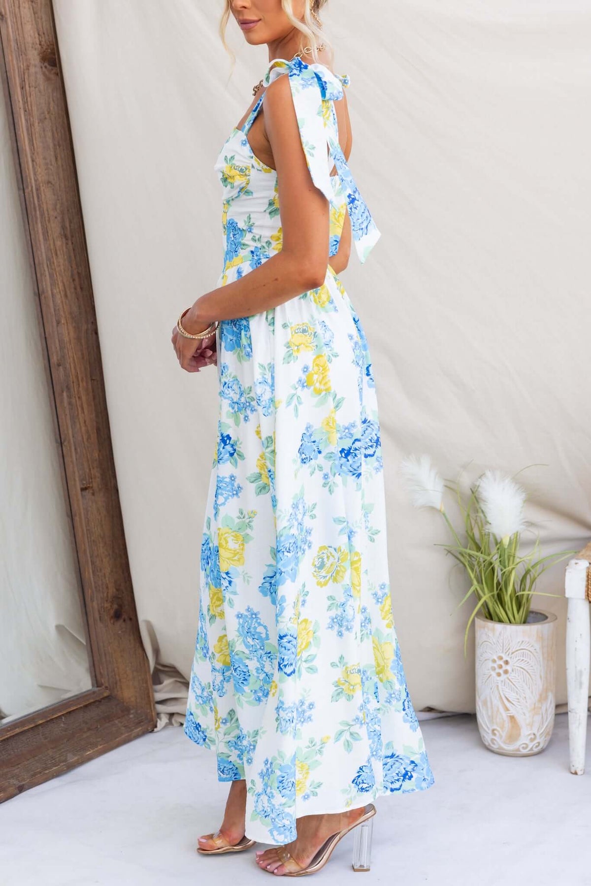 Woman wearing Rowena Maxi Dress with floral design, tie straps, and back zip, showcased in a bright setting.