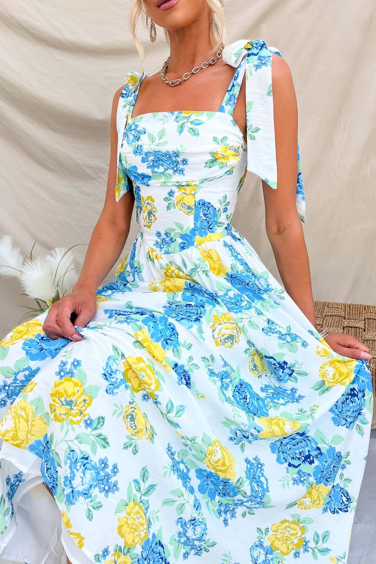 Rowena Maxi Dress featuring floral print with tie straps, elastic back zip, and a flowing skirt, styled in a relaxed setting.
