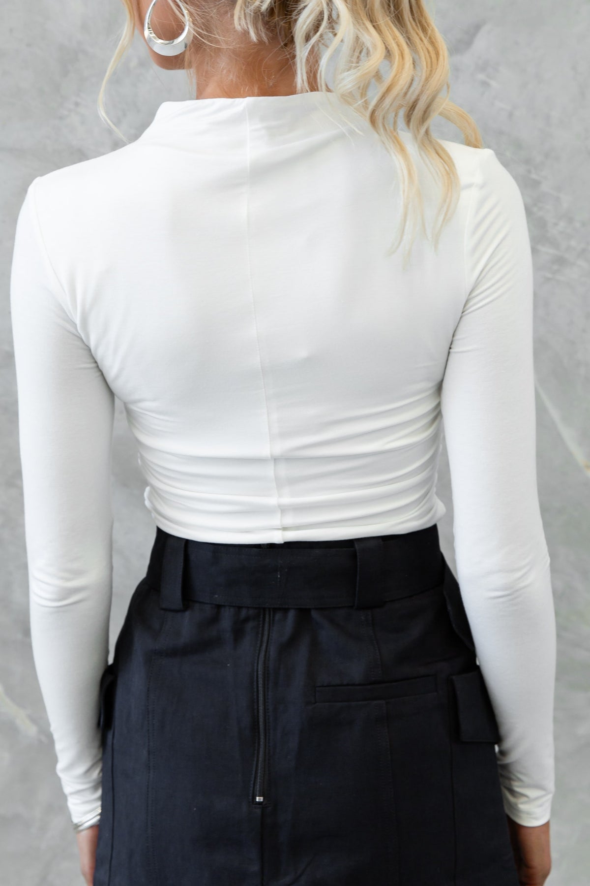 Back view of a woman wearing a white Rumba Top with long sleeves, showcasing a high neckline and fitted design.