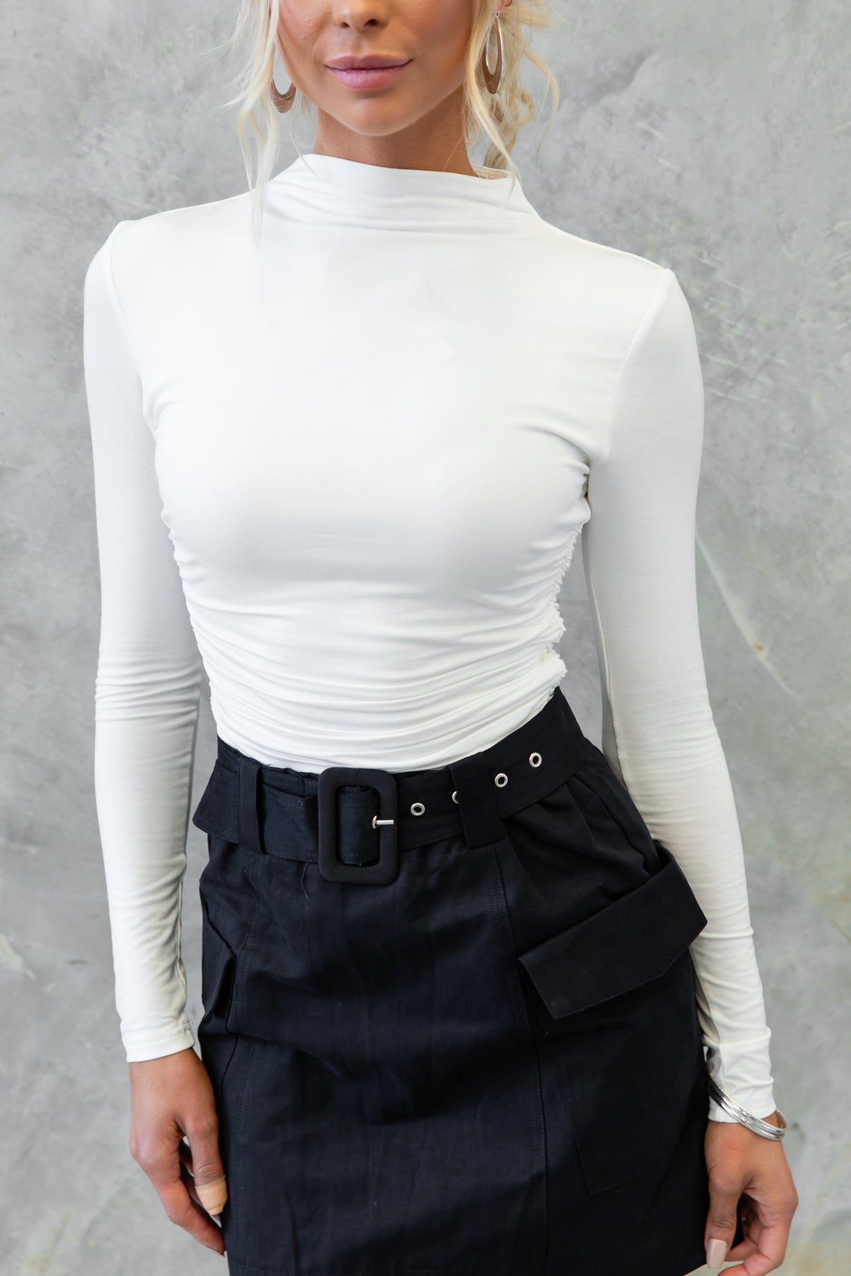 White high neckline Rumba Top with stretch fabric, styled with a black belted skirt.