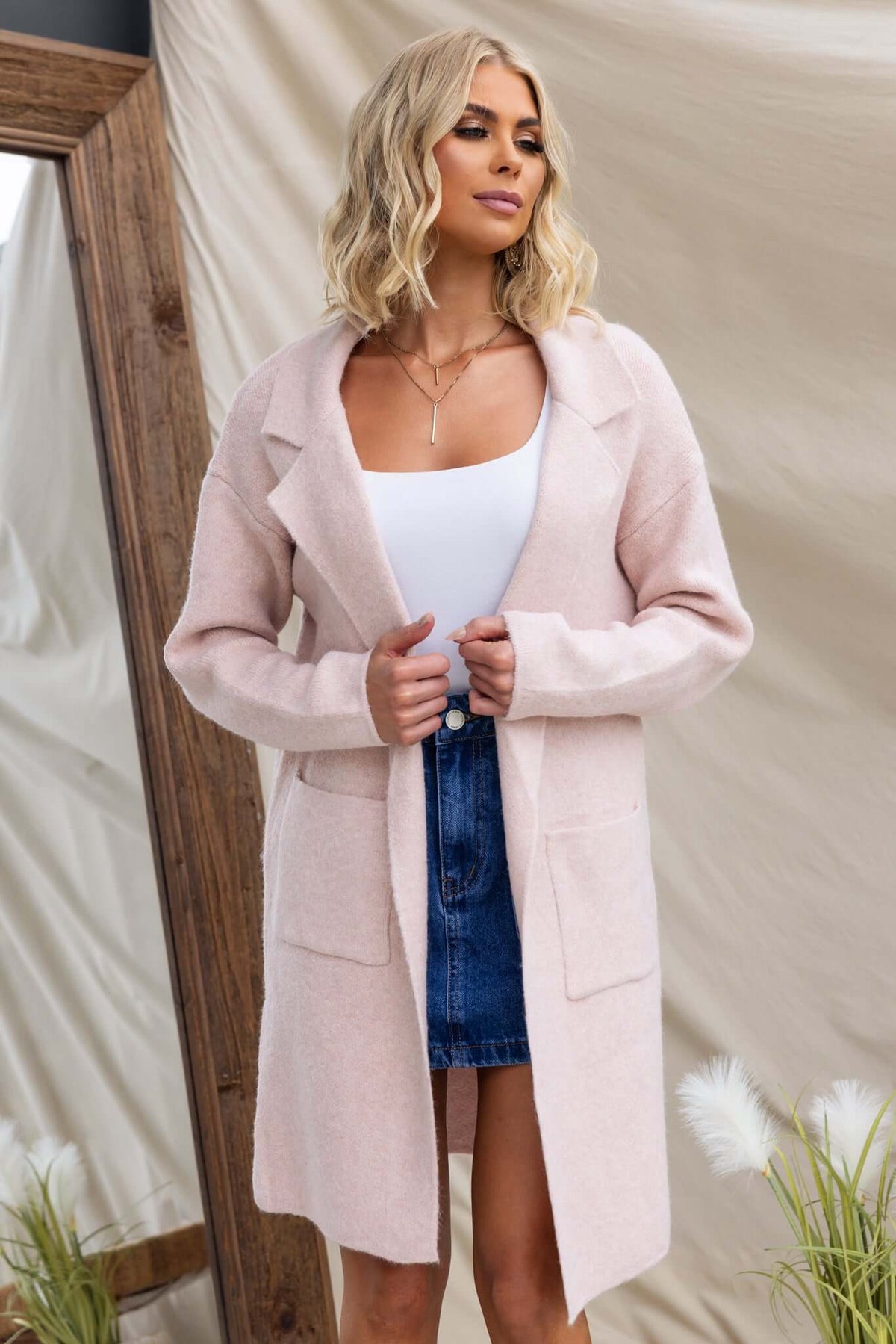 Model wearing a Sarlia Cardigan in light pink with pockets, styled over a white top and denim skirt.