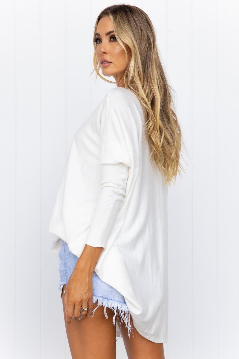 Model wearing the Bonnie Knit oversized top in white, styled with denim shorts, showcasing its relaxed fit and full-length sleeves.