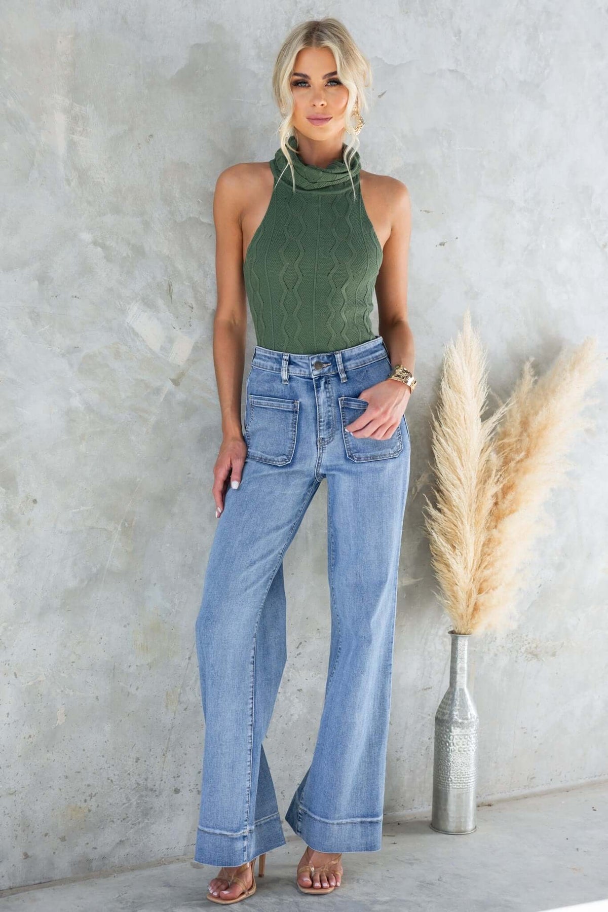 Model wearing a green Shannon bodysuit with a turtle neckline and wide-leg jeans against a textured background.