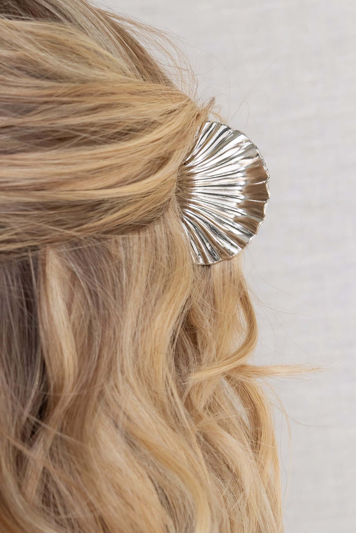 Shore claw clip with metallic finish holding back wavy blonde hair, 6cm length, ideal for stylish hairdos.