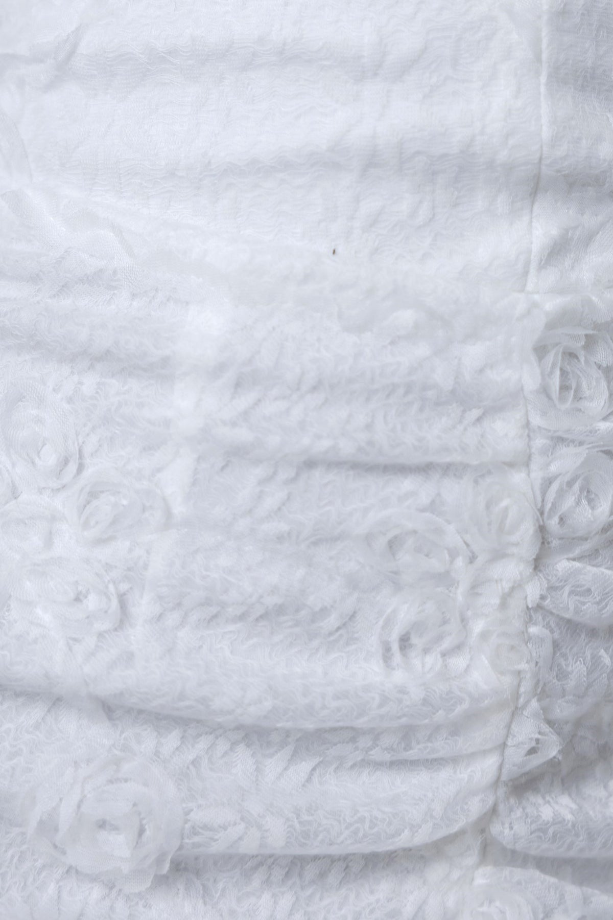 Close-up of textured white fabric featuring floral details, ideal for bridal wear and elegant dresses.