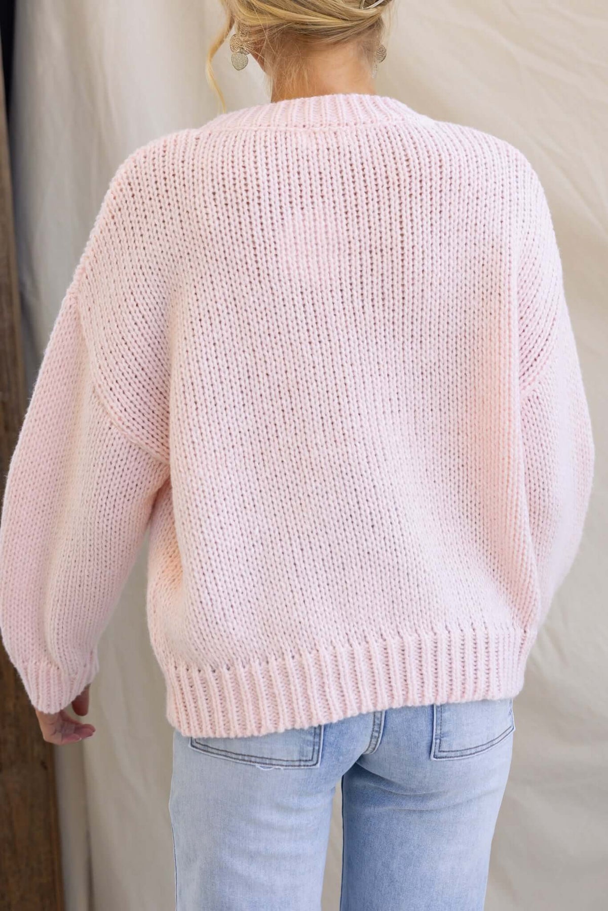 Back view of a pink knitted jumper with relaxed fit and round neckline, showing embroidered details and soft material.