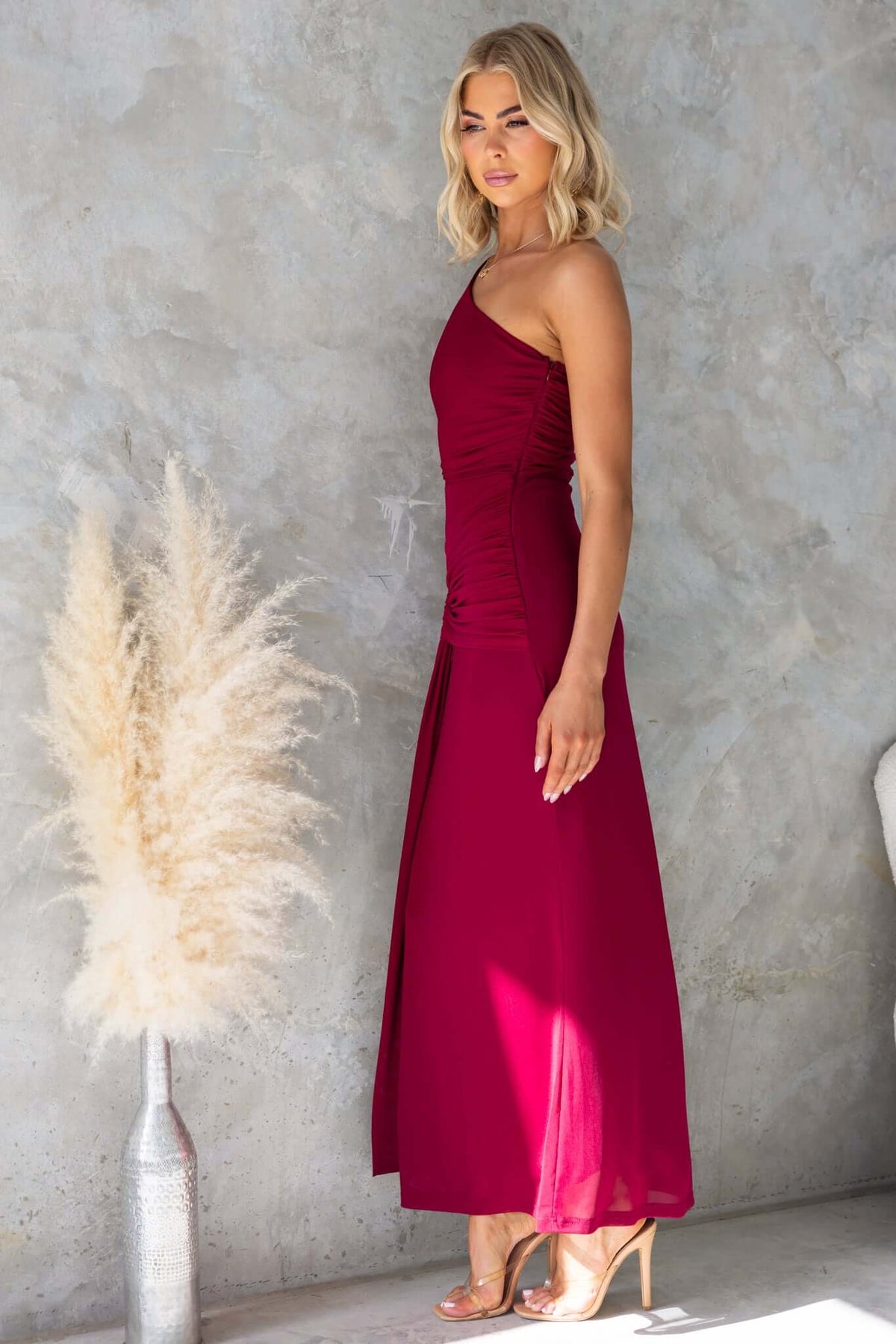 Model wearing a burgundy ultra maxi dress with a one-shoulder neckline and cut-out at the waist.