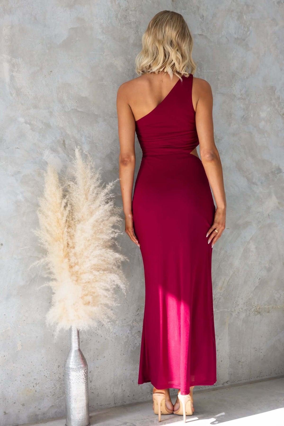 Model wearing a red one-shoulder maxi dress with cut-out waist detail, showcasing a stylish and elegant look.