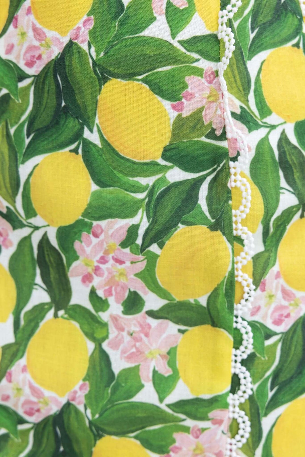 Close-up of Umeeka Dress fabric featuring vibrant lemons and pink flowers on a textured background.