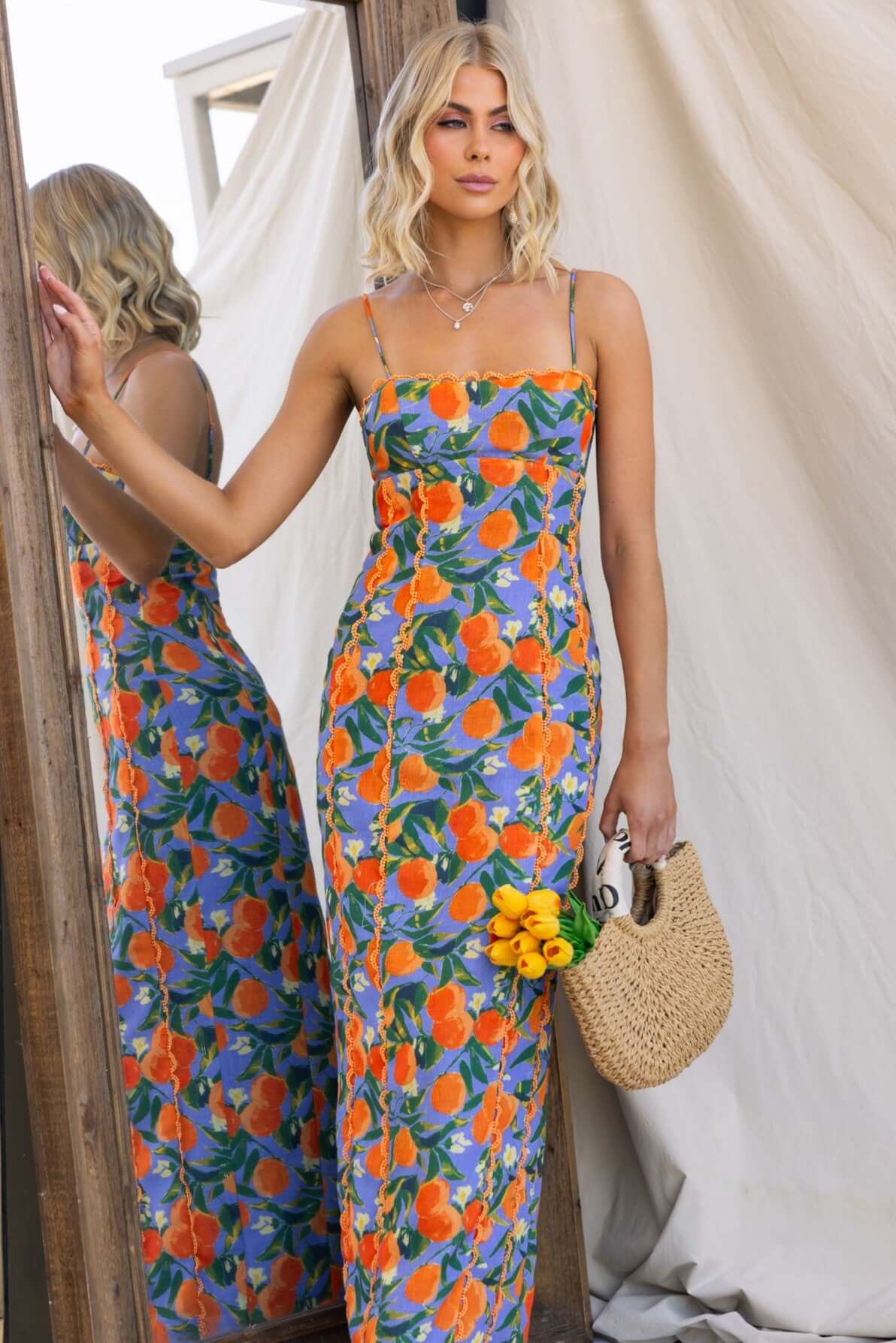 Umeeka Maxi Dress featuring floral design, adjustable straps, and back split, styled with a woven bag.