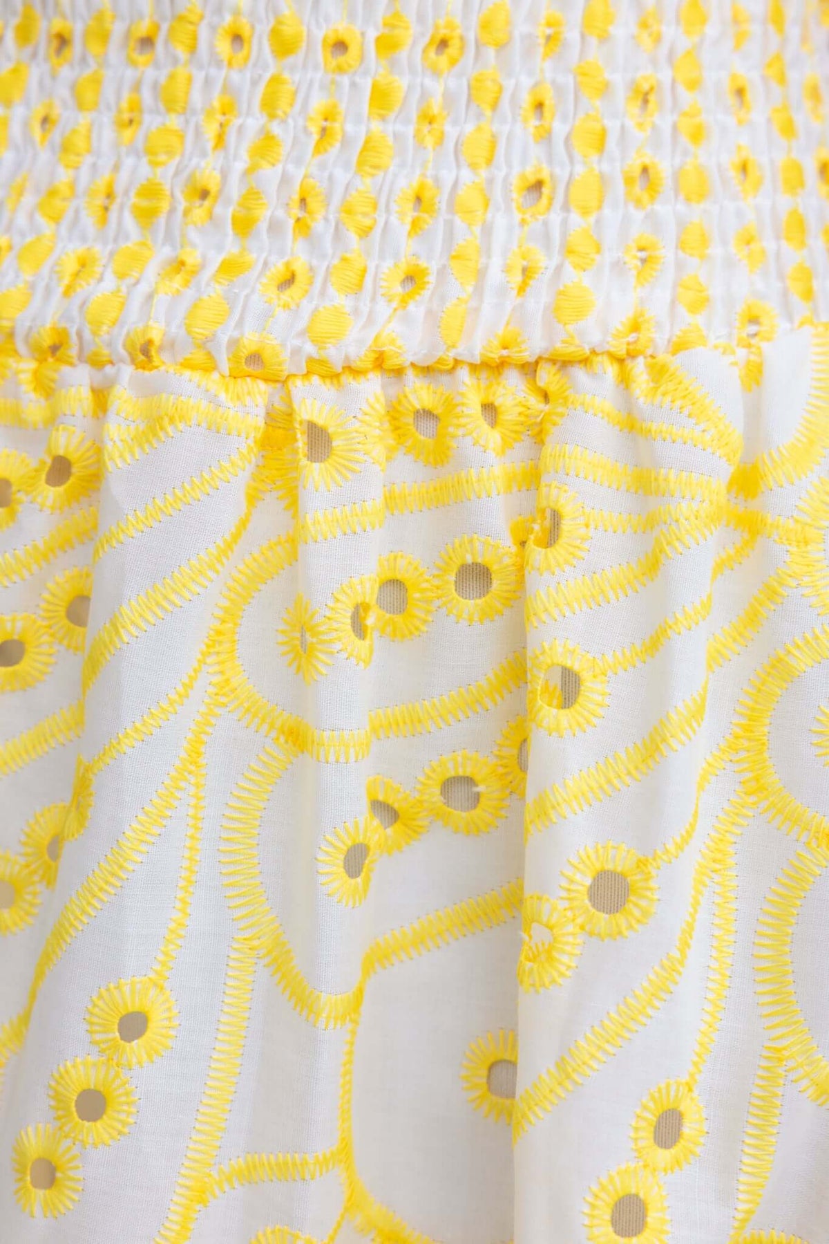 Close-up of Urena Midi Dress featuring yellow anglaise patterns on a white fabric, highlighting its elastic bodice and detailed design.