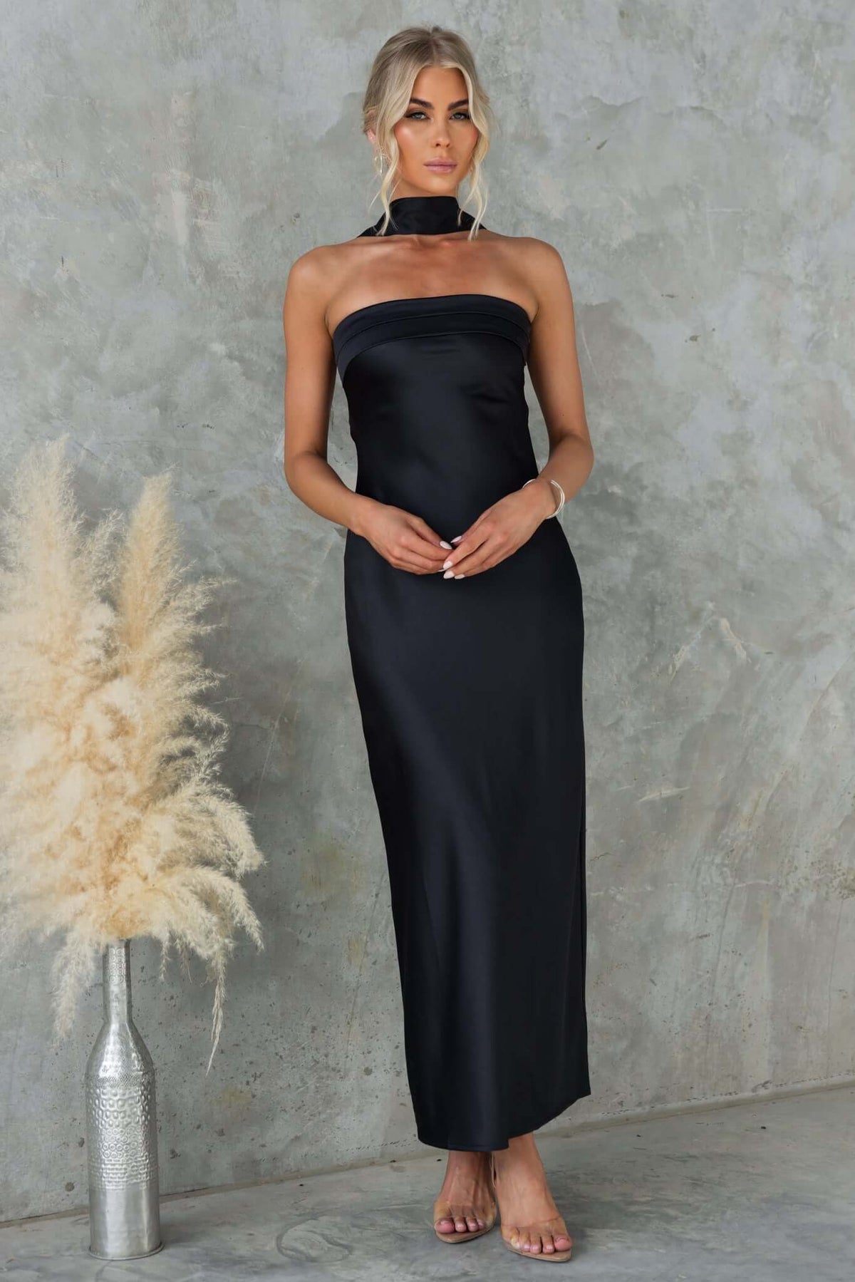 Black strapless Verda maxi dress with anti-slip, removable tie, and broach, modeled by a woman against a textured background.