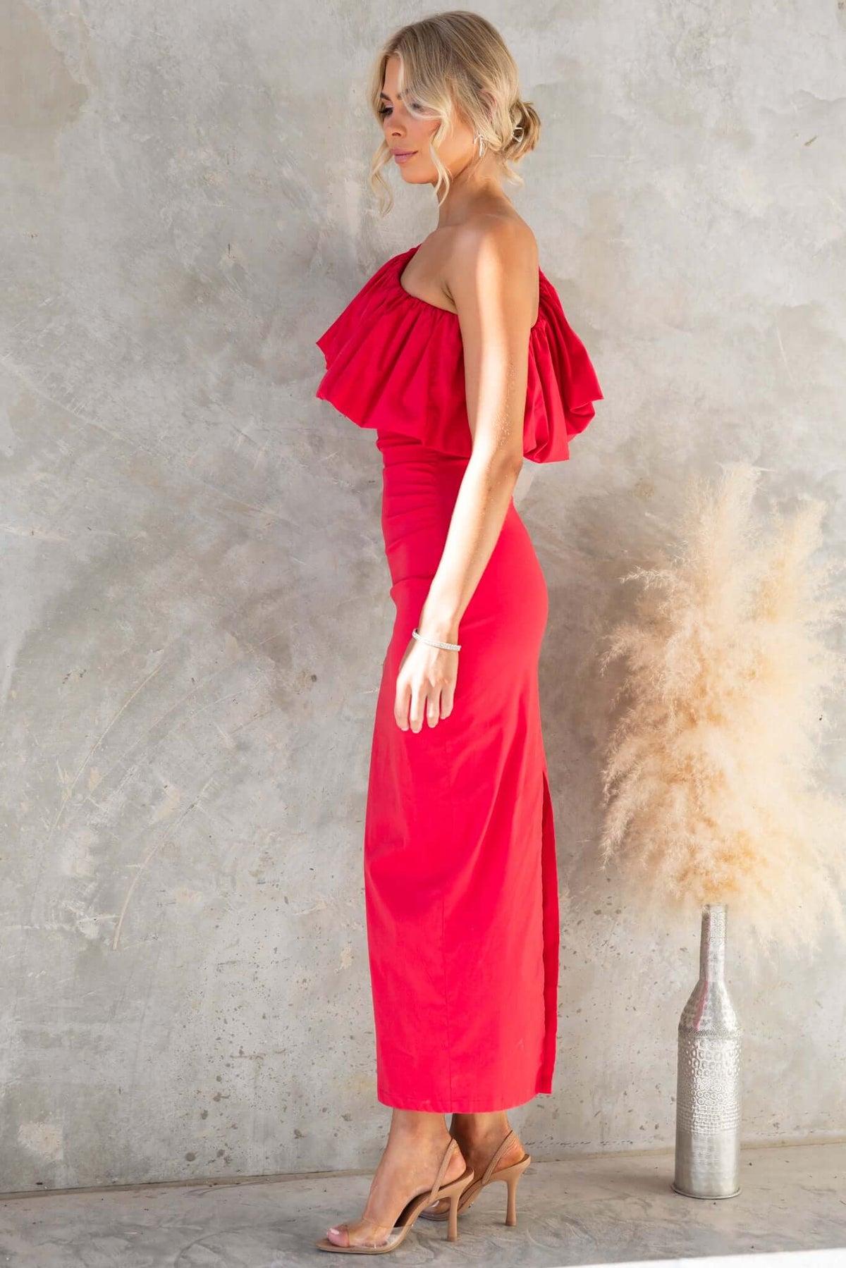 Model wearing the Vitoria Maxi Dress with one-shoulder neckline and split back, showcasing its vibrant red color.
