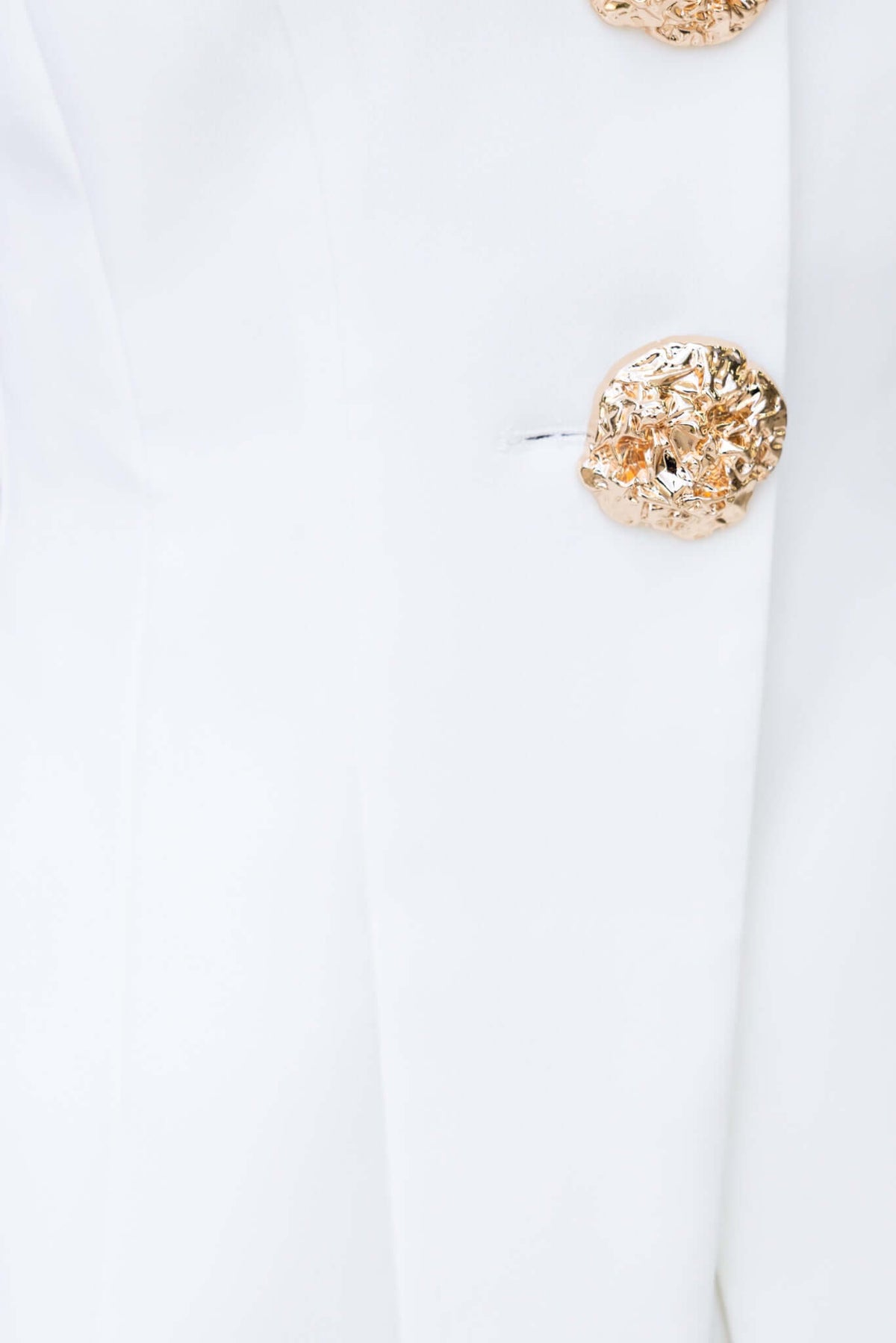 Close-up of elegant white garment featuring decorative gold buttons.