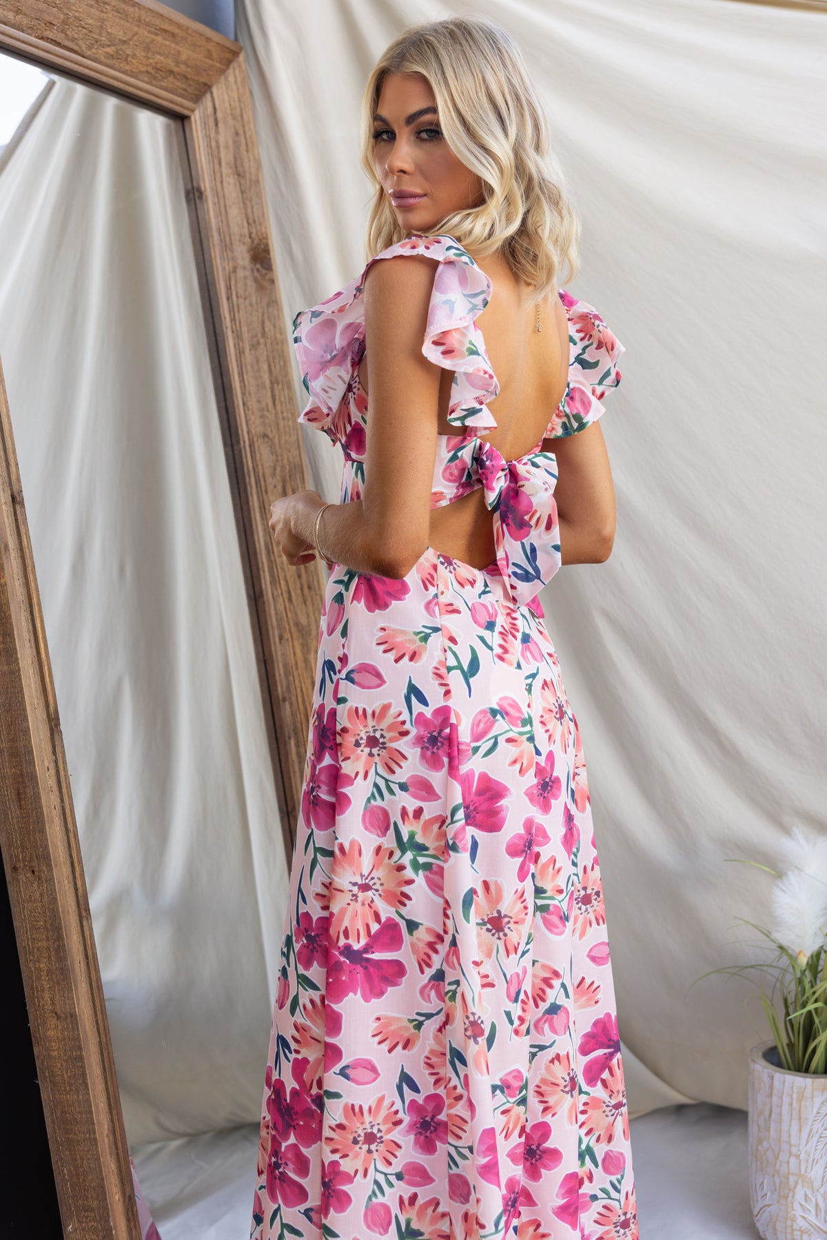 Model wearing a floral Wilma Maxi Dress, showcasing ruffled sleeves and tie back detail, seen from the back.
