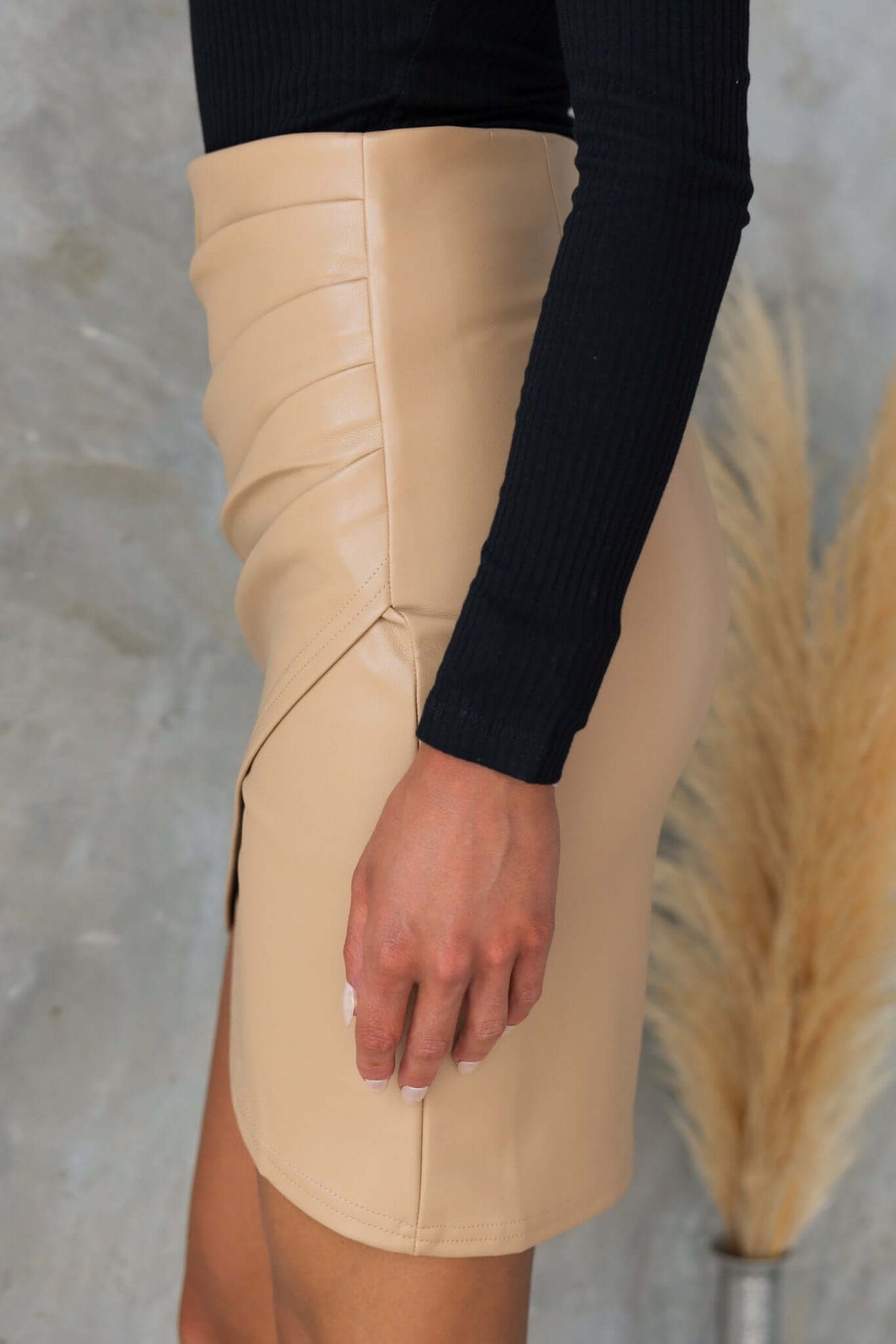 Side view of a faux leather Wylder skirt featuring pleat detail and an asymmetrical hemline.