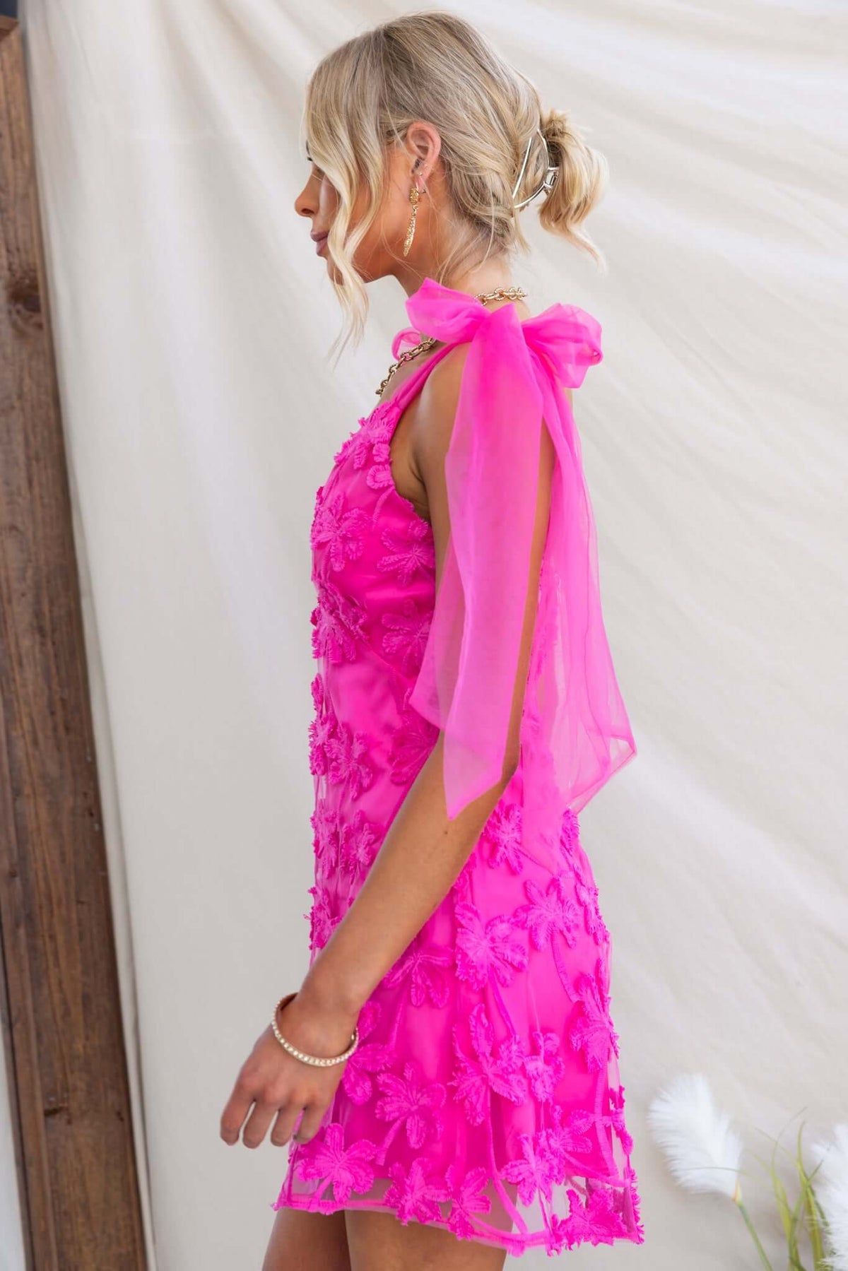 Model wearing the Xaria Dress in bright pink with tulle embroidery and tie straps, showcasing a stylish side profile.