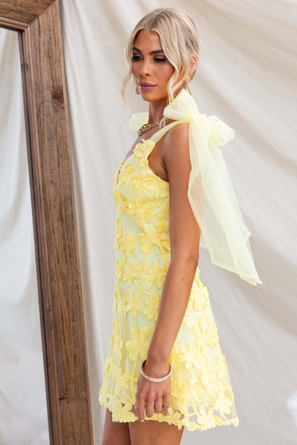 Xaria Dress in yellow with tulle flower embroidery and tie straps, showcased against a backdrop of soft fabric.