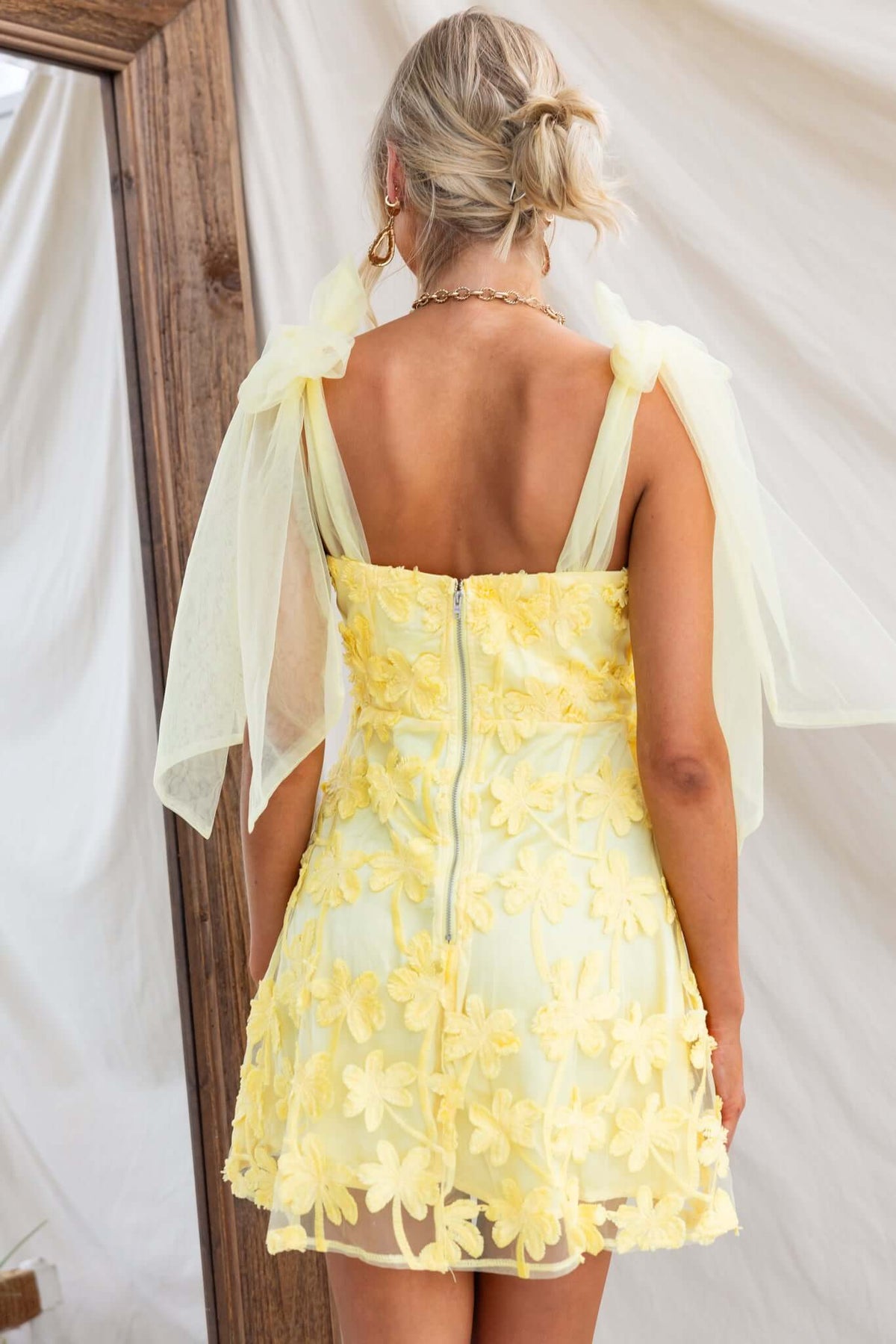 Back view of Xaria Dress featuring tulle embroidered material and tie straps in soft yellow color.